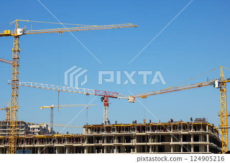 A bustling construction site is filled with cranes, complementing the clear blue sky above 124905216