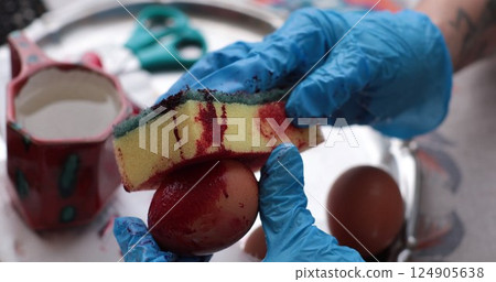 Creative process of coloring Easter eggs with red dye using a sponge technique in a cozy indoor setting during the festive spring season 124905638