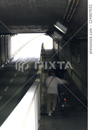 A pedestrian pushing a bicycle on the underpass 124907031