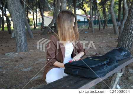 Girl Opens Case Of Bass Musical Instrument On Table In Park Among Trees 124908034
