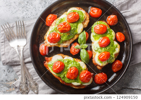 Chicken margherita is made with juicy pan-seared chicken, topped with basil pesto, mozzarella, roasted cherry tomatoes close-up on pan. Horizontal top view 124909150