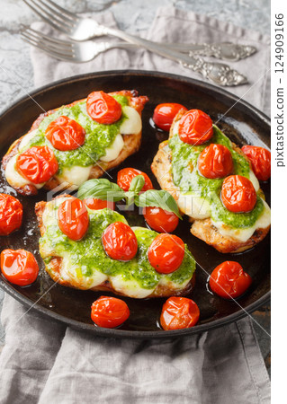 Margherita chicken that features pan-fried chicken breasts topped with melted mozzarella, pesto and tomatoes close-up on pan. Vertical 124909166