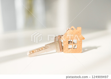 A house key with a keychain in the form of a wooden house on a light background A house key with a keychain in the form of a wooden house on a light background 124909497