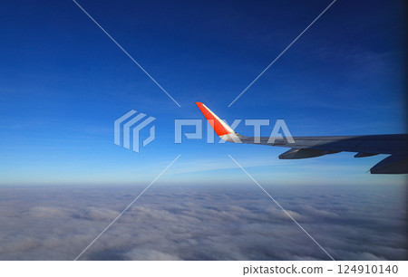 View from the airplane window at a beautiful cloudy sky and the airplane wing. Earth and sky as seen through window of an airplane. 124910140