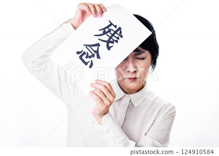 A middle-aged woman grimacing as she holds up a piece of paper with the word "regret" written on it A middle-aged woman grimacing as she holds up a piece of paper with the word "regret" written on it 124910584