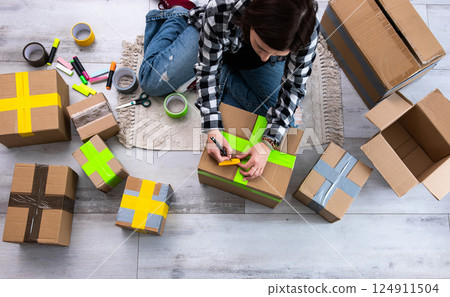 Girl Packs Cardboard Boxes And Seals Them With Tape At Home As She Prepares Them For Delivery 124911504