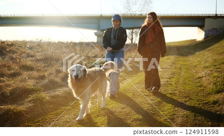 Mother And Daughter Walking With Golden Retriever Dog Outdoors At Sunset Mother And Daughter Walking With Golden Retriever Dog Outdoors At Sunset 124911598