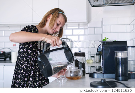 Cute Little Girl Brewing Tea Pouring Hot Water Into A Teapot In The Kitchen 124911620