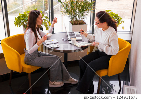 Caucasian businesswomen discussing future campaign ideas during coffee. Concept of online leadership and team innovation. Side view Caucasian businesswomen discussing future campaign ideas during coffee. Concept of online leadership and team innovation. Side view 124911675