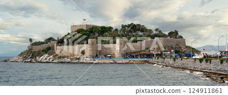 Kusadasi Castle overlooks the coastline and showcases historical architecture under a cloudy sky Kusadasi Castle overlooks the coastline and showcases historical architecture under a cloudy sky 124911861