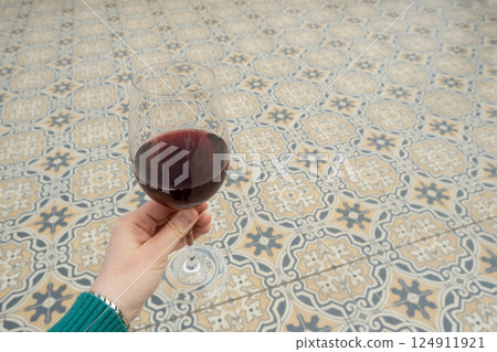 A glass of red wine in a womans hand on a background of beautiful tiles, space for text A glass of red wine in a womans hand on a background of beautiful tiles, space for text 124911921
