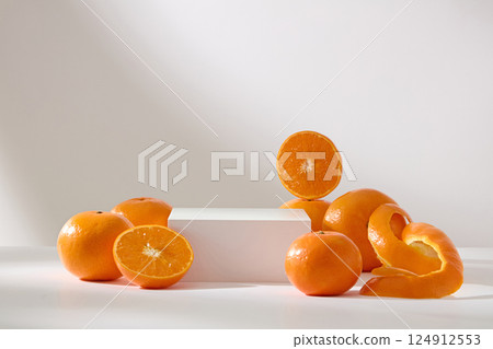 Frontal shot of a rectangular podium on white background. Fresh orange cut in half to reveal juicy flesh. Orange peel is thinly sliced to spirals. Empty space for showing product or designing. Frontal shot of a rectangular podium on white background. Fresh orange cut in half to reveal juicy flesh. Orange peel is thinly sliced to spirals. Empty space for showing product or designing. 124912553