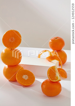 Rectangular white podium used to place the products. Oranges are cut into segments to reveal white fibers, and peels are cut into long strips. The oranges are stacked on top of each other. 124912559