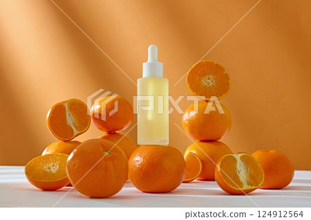 Dropper bottles placed on oranges with rough skin. Cosmetic bottles extracted from natural ingredients, unlabeled for designing. Oranges cut in half lying around, displayed on a white plate. 124912564