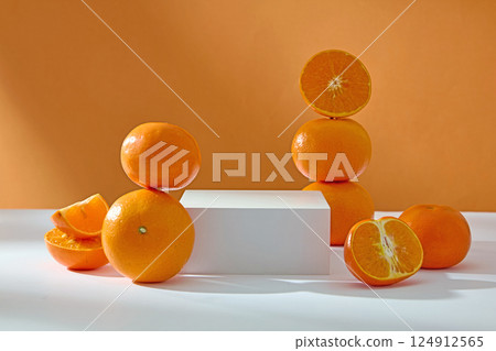 Oranges cut in half to expose white fiber between the segments. Several oranges arranged vertically around a rectangular white podium. Brown background. Empty space for showing products. Oranges cut in half to expose white fiber between the segments. Several oranges arranged vertically around a rectangular white podium. Brown background. Empty space for showing products. 124912565