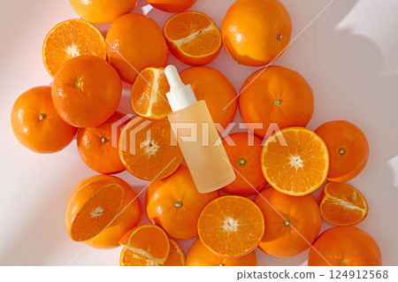 Flat lay shot of a cosmetic dropper bottle. Oranges are arranged randomly on a white background, some of them cut in half and into segments. Photo used in a natural cosmetics advertising visual Flat lay shot of a cosmetic dropper bottle. Oranges are arranged randomly on a white background, some of them cut in half and into segments. Photo used in a natural cosmetics advertising visual 124912568