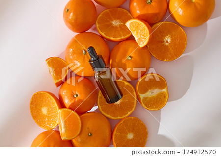 Unlabeled amber dropper serum bottles for advertising, placed on oranges lying randomly. Oranges cut into various shapes are lying next to each other. Oranges have many uses in cosmetics and beauty. 124912570