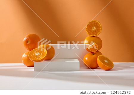 A low, rectangular white podium is positioned beside a taller podium, creating an empty space to highlight the product. Soft lighting shines in and the shadows of the oranges show on the table A low, rectangular white podium is positioned beside a taller podium, creating an empty space to highlight the product. Soft lighting shines in and the shadows of the oranges show on the table 124912572