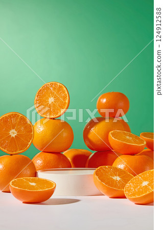 A round white pedestal emerges between stacks of vibrant oranges. Sliced orange revealing fresh orange segments and oranges cut in half placed everywhere. Vertical photo. Green background. 124912588