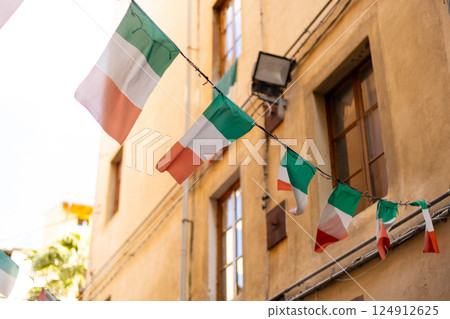Typical street with houses in Italy. Facade of a yellow building with Italian flags. Italian flag in an old town narrow street of a city in Italy 124912625
