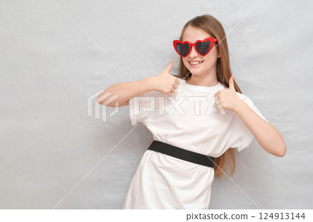 Caucasian young girl with heart-shaped sunglasses giving thumbs up in casual Caucasian young girl with heart-shaped sunglasses giving thumbs up in casual 124913144
