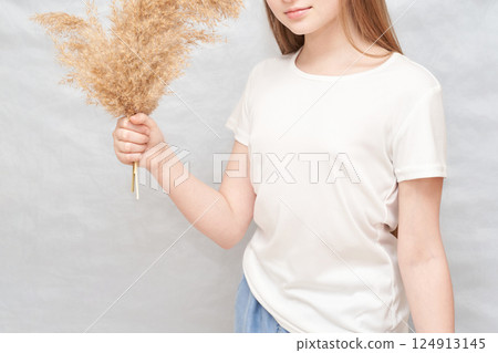 Young caucasian female holding dried pampas grass in casual white t-shirt 124913145