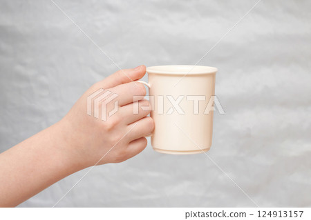 Close-up of female caucasian hand holding white ceramic mug against neutral Close-up of female caucasian hand holding white ceramic mug against neutral 124913157
