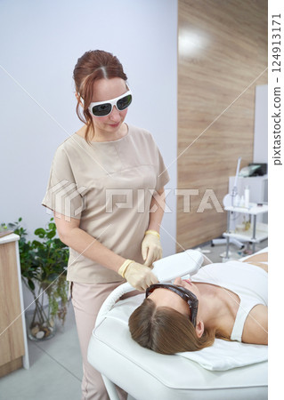 Female spa professional performing laser treatment on young caucasian woman Female spa professional performing laser treatment on young caucasian woman 124913171