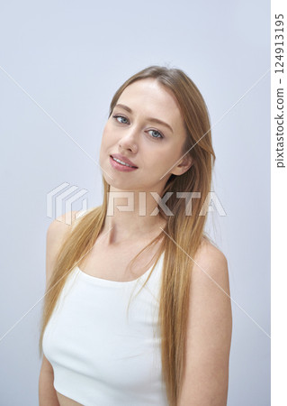 Young caucasian female with long hair in white top against light blue background Young caucasian female with long hair in white top against light blue background 124913195