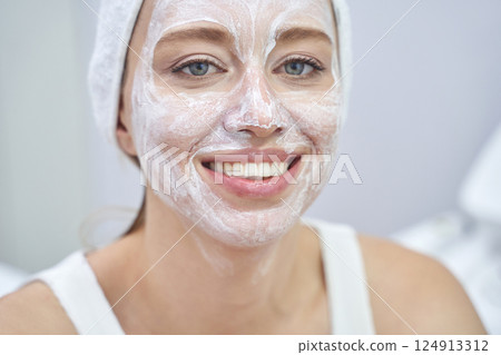 Caucasian female adult with facial mask smiling in spa setting for skincare 124913312