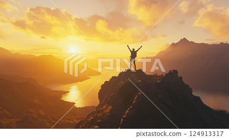 Silhouette of a climber feeling victorious on the summit at sunset 124913317