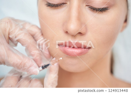 Young caucasian female receiving lip filler injection by gloved hands Young caucasian female receiving lip filler injection by gloved hands 124913448