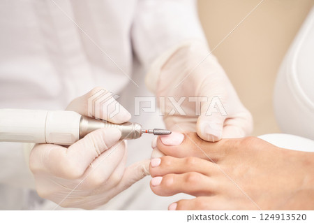 Professional pedicure treatment on female feet with machine tool by gloved 124913520