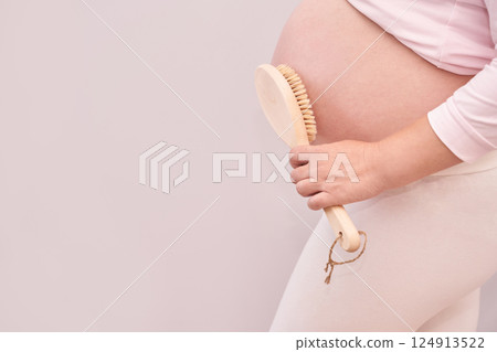 Pregnant caucasian woman exfoliating belly with body brush for skincare routine 124913522