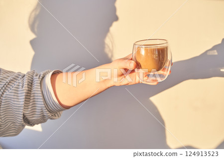 Female hand holding coffee cup creating shadow against sunlit wall 124913523