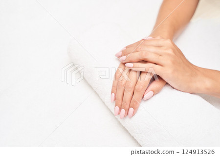 Female hands with neutral nail polish resting on white towel with clean 124913526