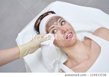 Young caucasian female undergoing facial treatment with carbon mask in spa Young caucasian female undergoing facial treatment with carbon mask in spa 124913536