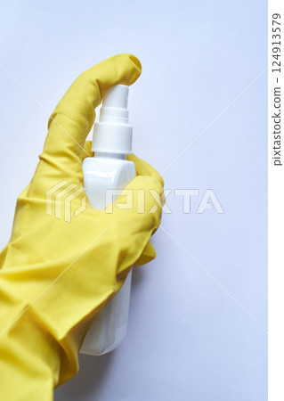 Hand in yellow glove holding white spray bottle against clean white background 124913579