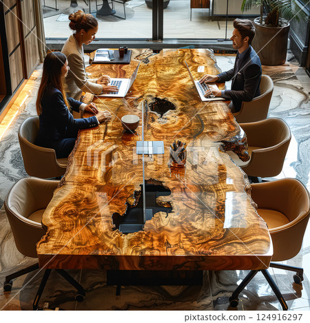 Group of people are sitting at a long wooden table, working on their laptops 124916297