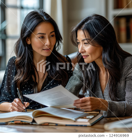 Two women are sitting at a table, one of them writing in a book 124916969