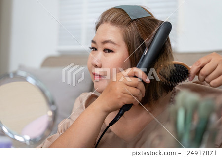 Beauty Routine and Hair Styling. A woman straightening her hair in front of a mirror, preparing for her day. Beauty Routine and Hair Styling. A woman straightening her hair in front of a mirror, preparing for her day. 124917071