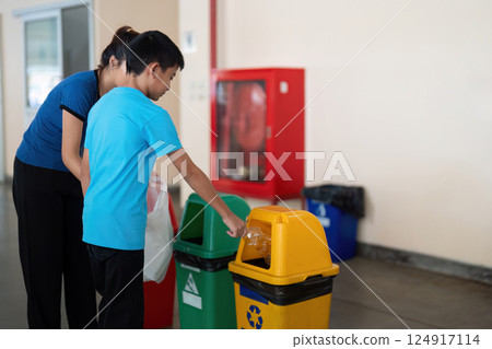 Recycling and Education. A child learns about recycling while disposing of waste properly with the help of a caregiver. 124917114