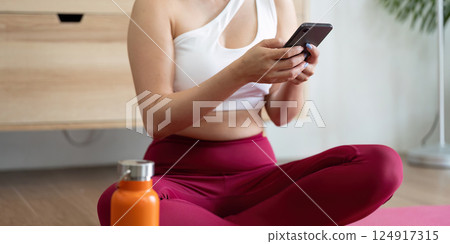 Hydration and Self-Care. A woman checking her phone after a yoga session, highlighting the importance of hydration and wellness. 124917315