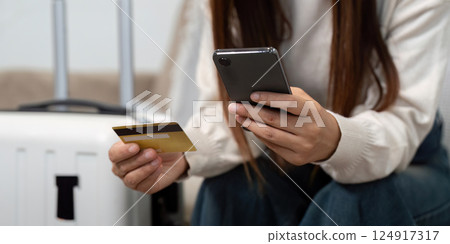 Travel Planning and Digital Convenience. A woman checks travel details using her smartphone and credit card. Travel Planning and Digital Convenience. A woman checks travel details using her smartphone and credit card. 124917317