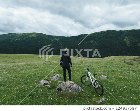 Aerial view of woman riding mountain bike on flowering grassland mountain trail Aerial view of woman riding mountain bike on flowering grassland mountain trail 124917587