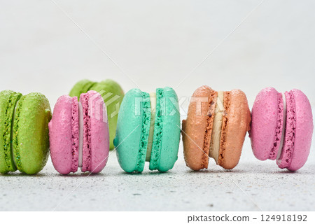 An assortment of colorful macarons on a white surface with dark speckles. The macarons have a smooth, delicate shell and a creamy filling 124918192