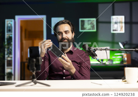 Content creator informing audience about newly launched mini soundbar. Man in studio holding high end music playing device, filming opinions with cellphone on tripod stabilizer Content creator informing audience about newly launched mini soundbar. Man in studio holding high end music playing device, filming opinions with cellphone on tripod stabilizer 124920238
