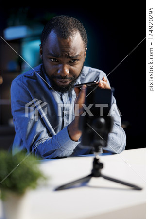 Content creator using smartphone on phone holder as recording gear to shoot intro for vlog channel on online platforms. Internet star warmly welcoming dedicated fanbase, filming with cellphone Content creator using smartphone on phone holder as recording gear to shoot intro for vlog channel on online platforms. Internet star warmly welcoming dedicated fanbase, filming with cellphone 124920295