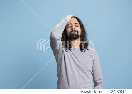 Worried hopeless guy feeling disappointed and depressed on camera, being gloomy with regret against blue background. Young stressed man deals with sorrow and misfortune, failure. 124920343