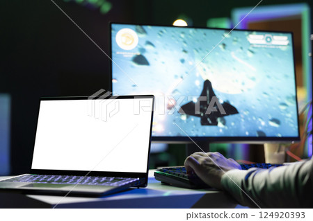 Isolated screen laptop next to man playing with friends online, shooting asteroids together in spaceship flying game. Mockup notebook next to gamer cooperating with teammates in coop videogame 124920393